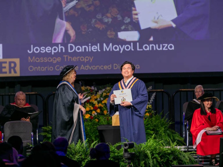 Massage Therapy graduate Joseph Daniel Mayol Lanuza smiles on stage with certificate