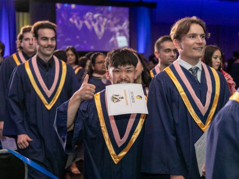 Graduate biting his certificate holds thumbs up to camera