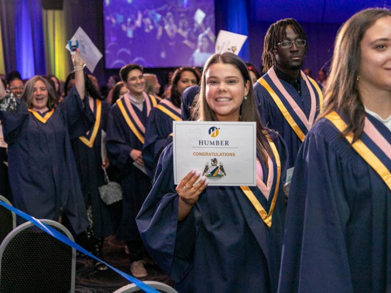Graduates smiles at camera as she leaves the ceremony hall