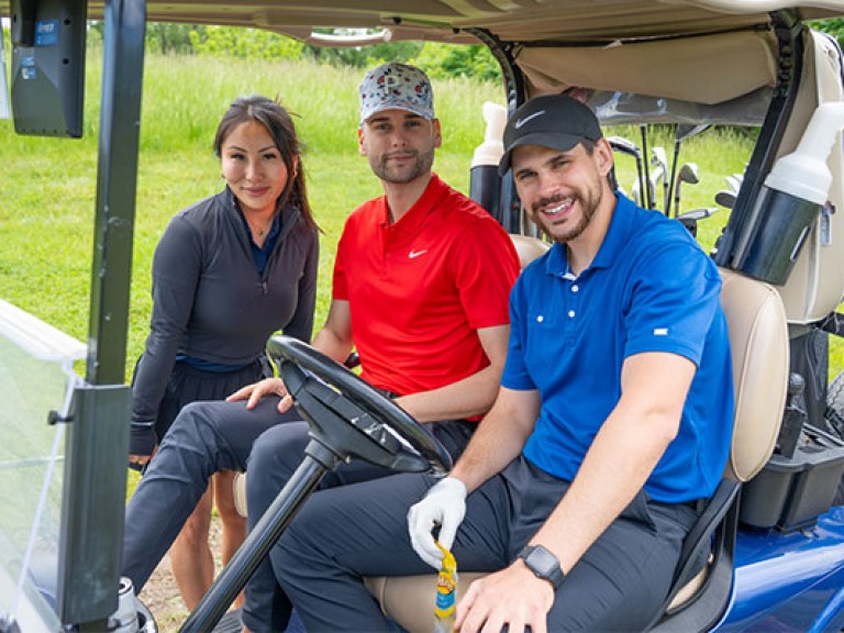 three people posing on a golf cart