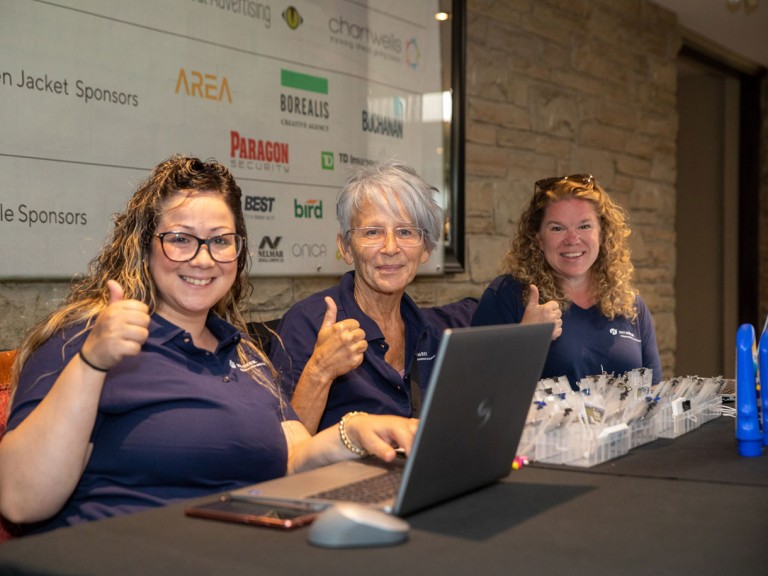 Three people at table smiling for camera holding thumbs up