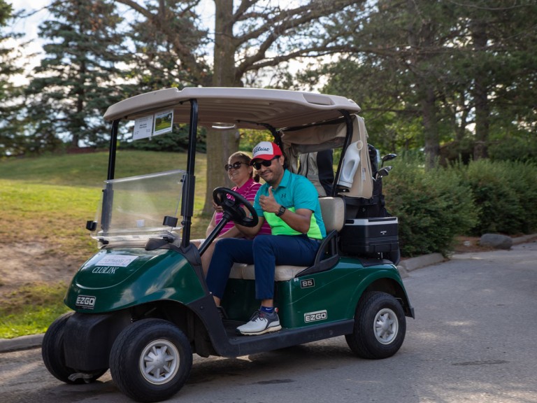 Driver of a golf cart holds thumbs up for camera