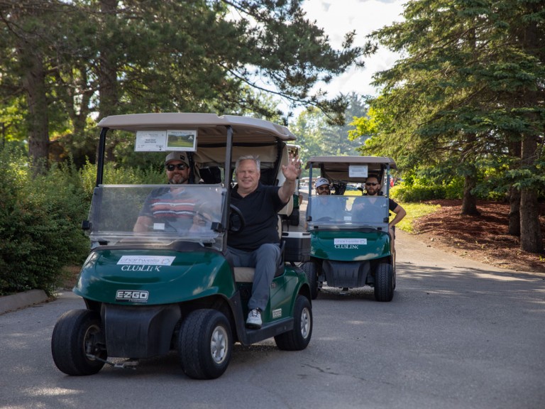 Driver of golf cart waves towards photographer