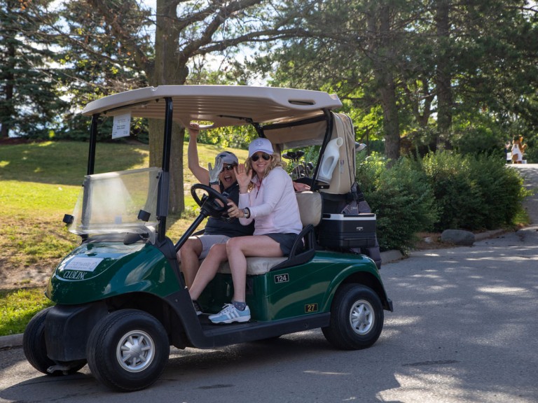 Two people in golf cart wave
