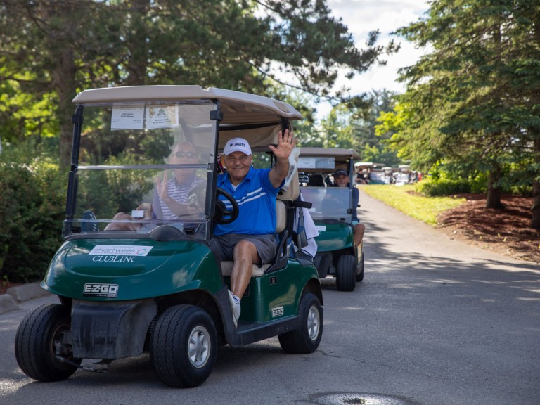 Driver of golf cart waves at camera