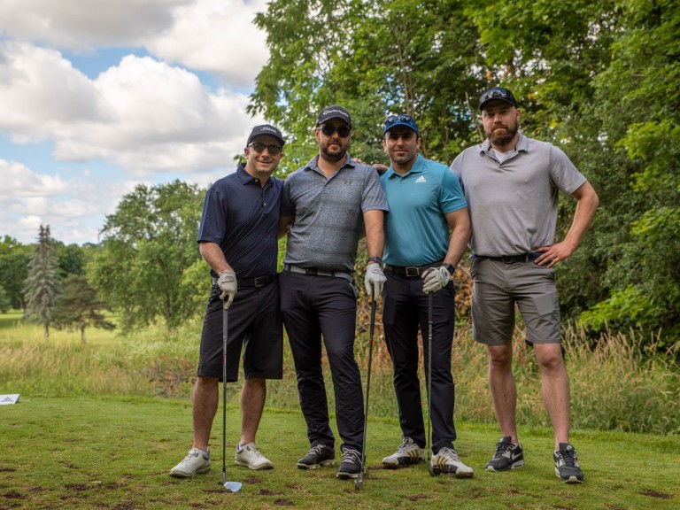 Four people in golf gear holding clubs pose for camera