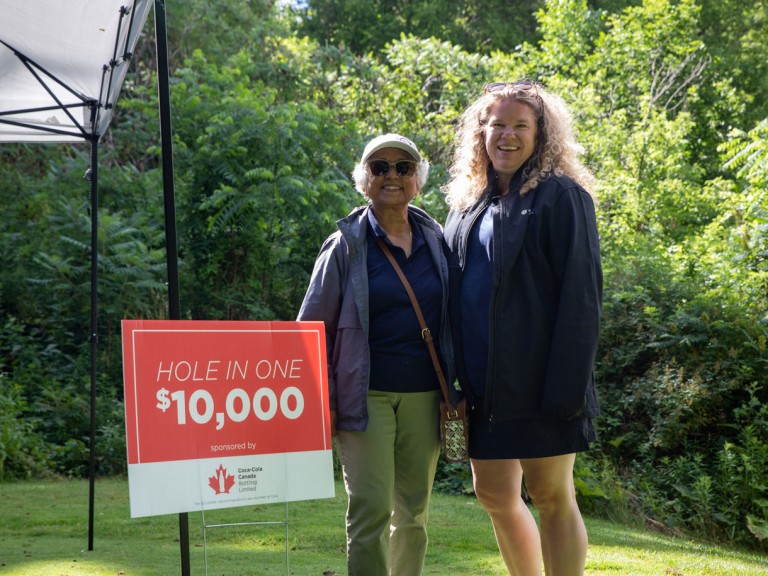 Two people smiling next to a sign that reads: hole in one $10 000