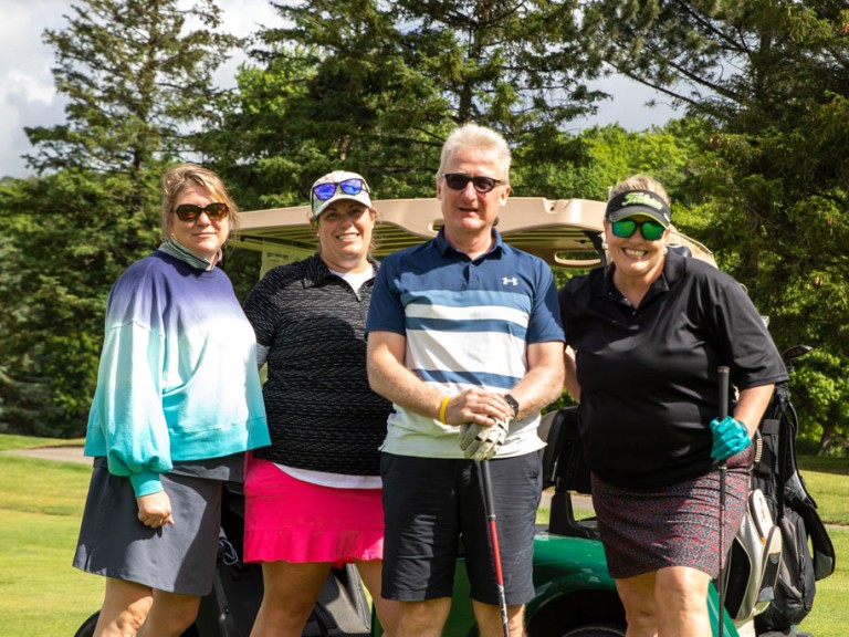 Four people smile in front of their golf cart on the grass