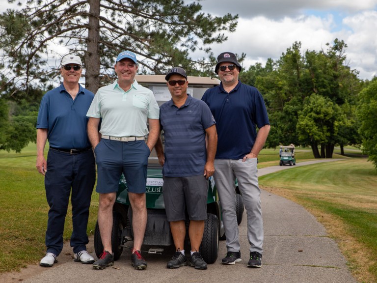 Four people smile in front of their golf cart on the paved path