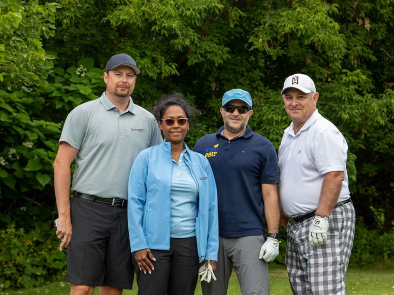 Four people smile for camera in front of trees