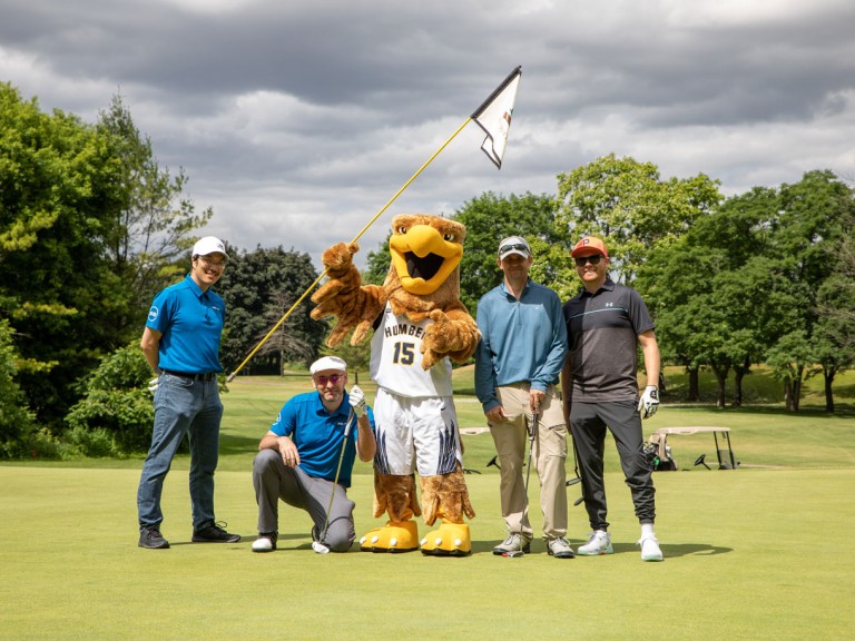Four people pose on course with Humber mascot