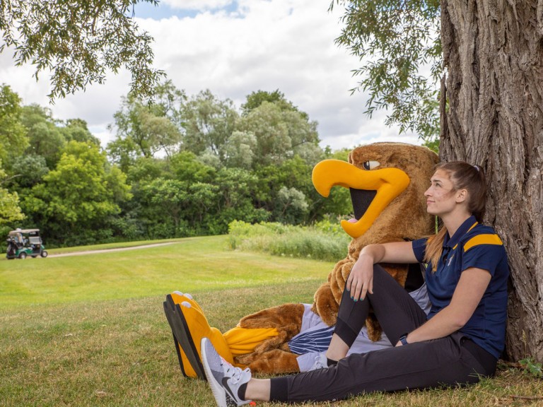 Person with Humber mascot sitting at base of tree