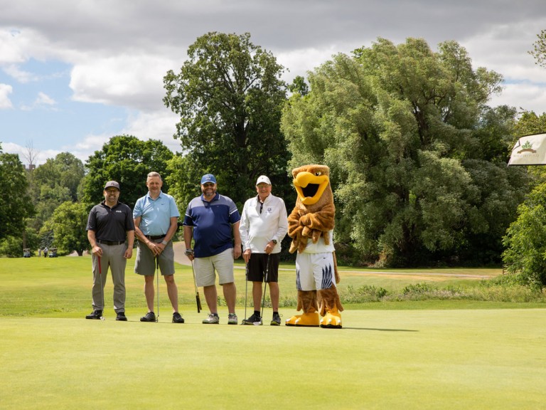 Four people pose next to Humber mascot