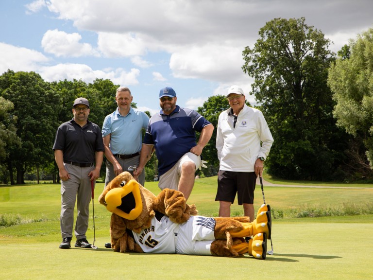 Four people pose behind Humber mascot who's lying on ground