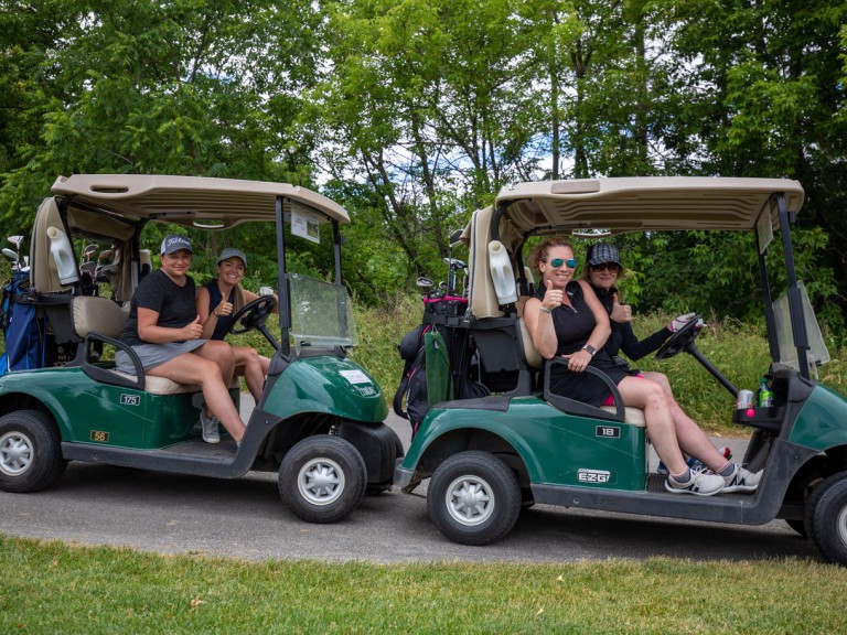 Two golf carts with drivers and passengers holding thumbs up