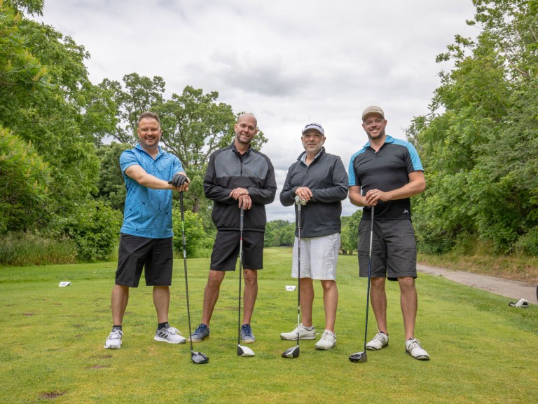 Four people pose with hands resting on top of clubs
