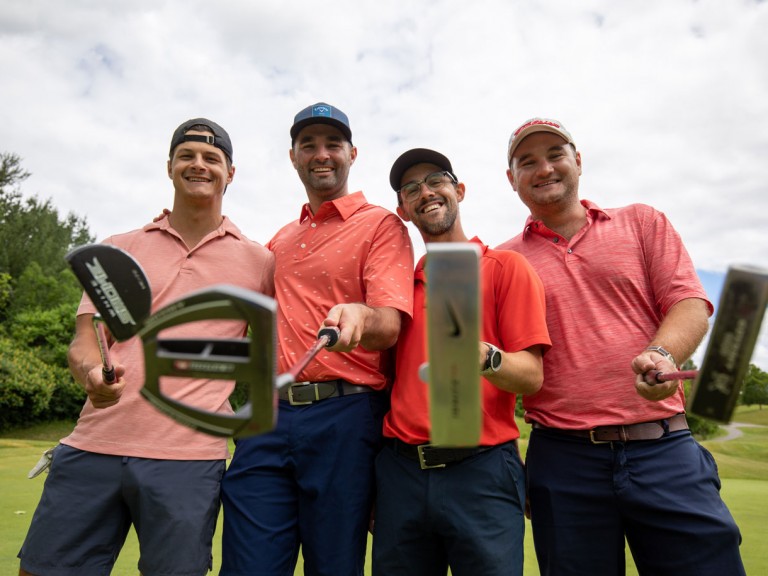 Four people in similar pink shirts hold clubs towards camera
