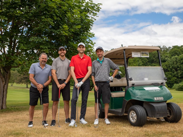 Four people pose near golf cart
