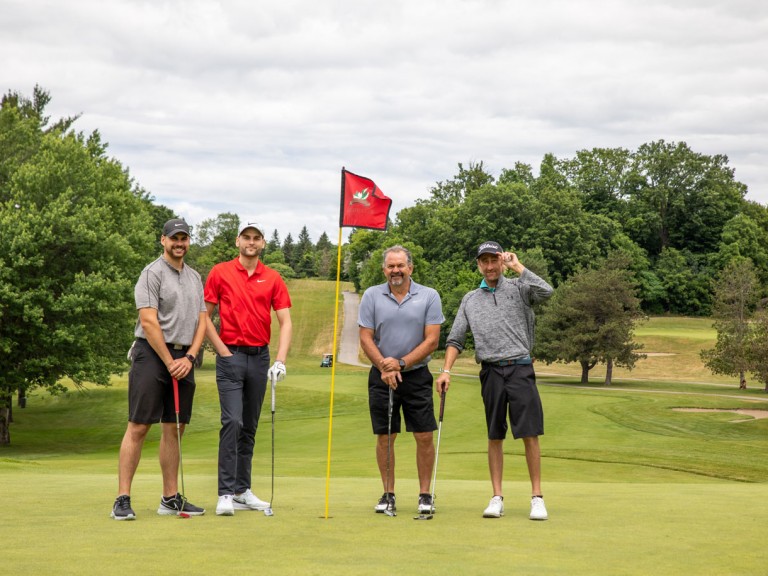 Four people pose with flag of hole in the middle