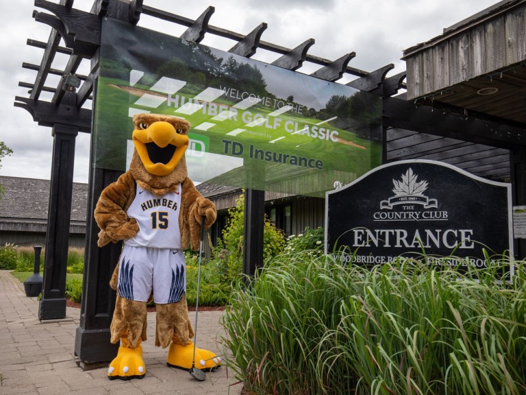Humber mascot stands in front of country club entrance