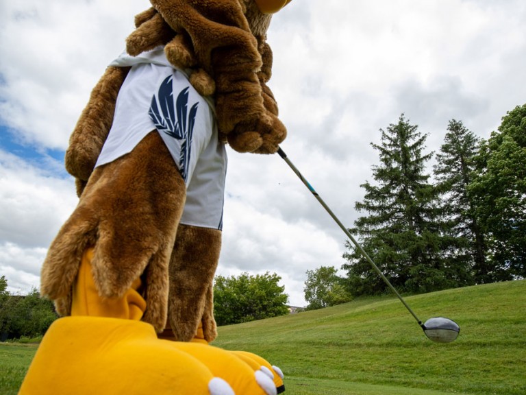 Humber mascot holding club near golf ball