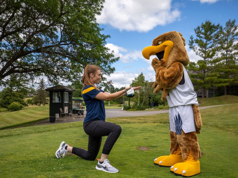 Person kneeling offering Humber mascot a golf ball as if it were a marriage proposal