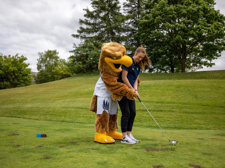 Humber mascot behind person helping them aim their club