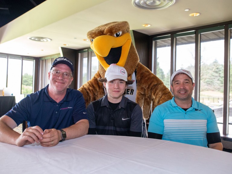Three people sitting at table with Humber mascot behind them