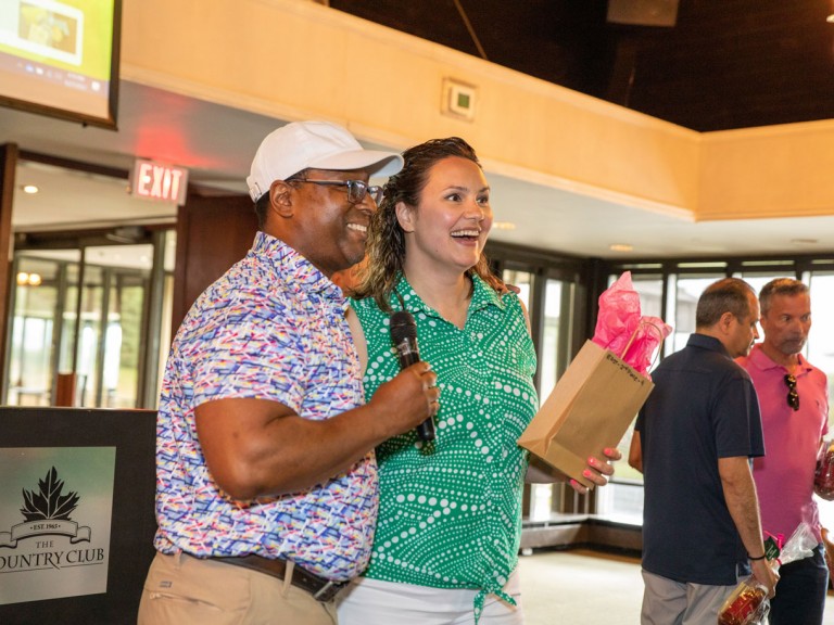 Person with microphone smiling next to person holding gift bag
