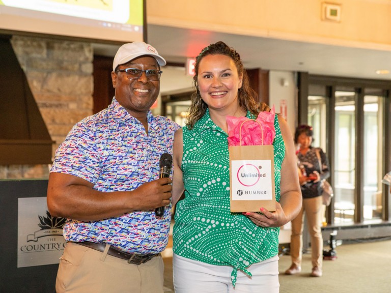 Person with microphone smiling next to person holding gift bag