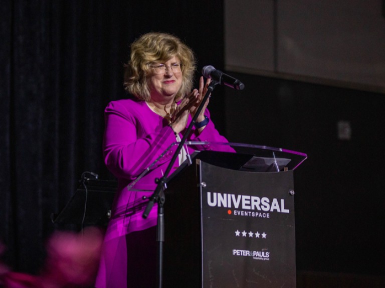 Humber president Ann Marie Vaughan clapping behind podium microphone