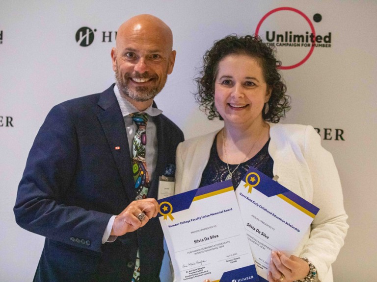 Two people posing in front of Humber Unlimited backdrop wall with awards