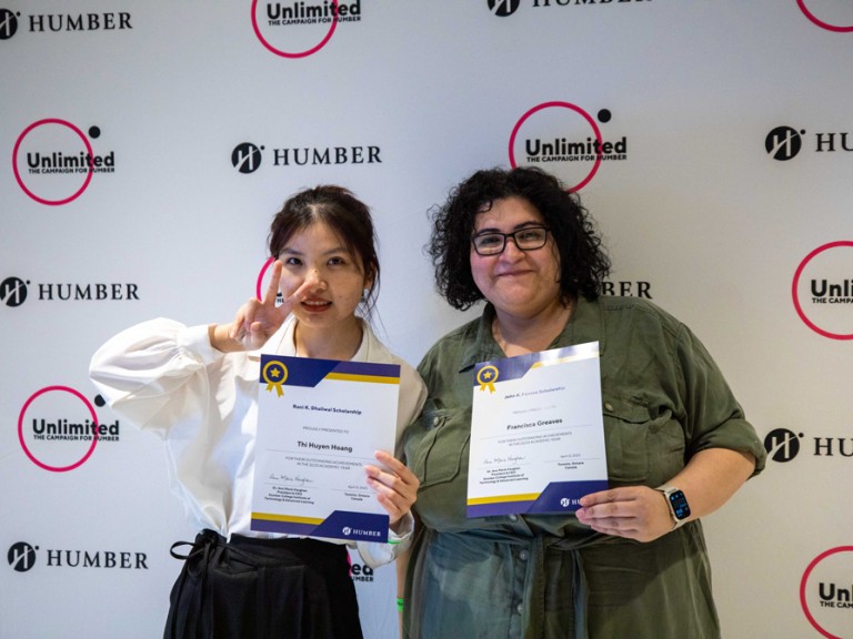 Two people holding their awards in front of Humber Unlimited backdrop wall