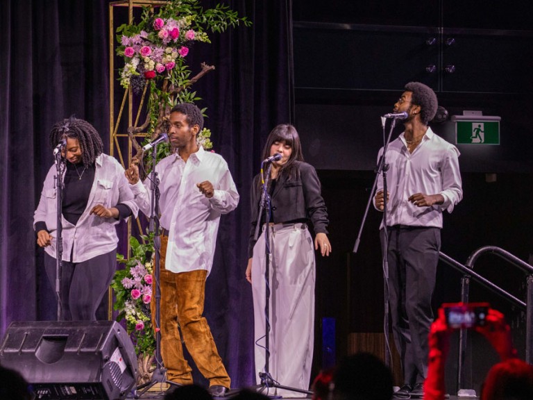 Four people on stage singing into microphones