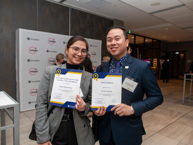 Two scholarship recipients smile for photo with their awards