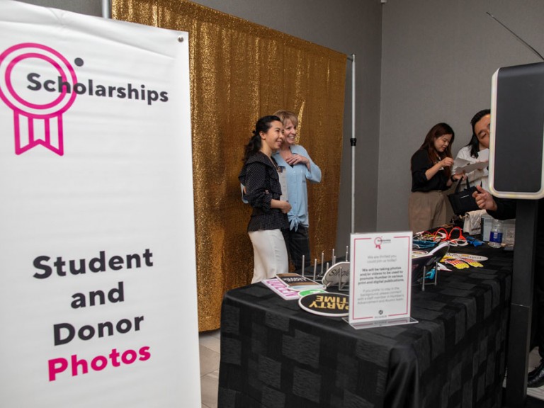 Two people take photo in front of Student and Donor Photos wall