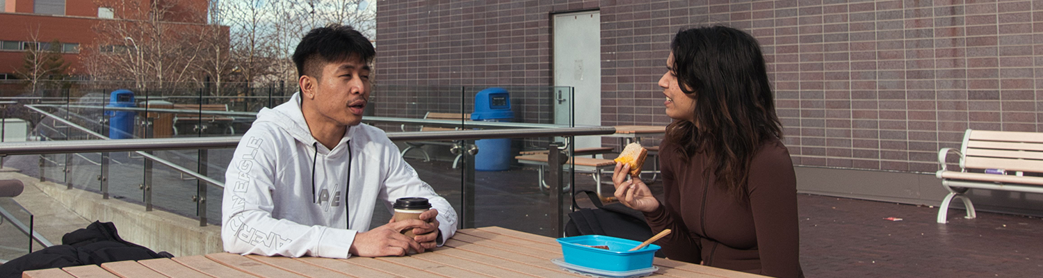 two people sitting outside drinking coffee and eating lunch