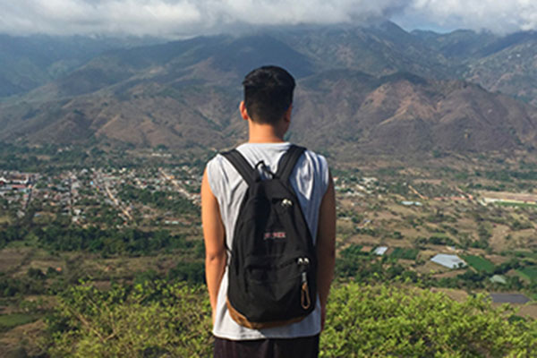 student with his back facing the camera looking out towards a mountain