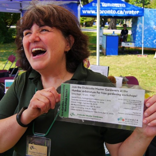 A smiling woman holds up a flyer for free gardening workshops at the Arboretum