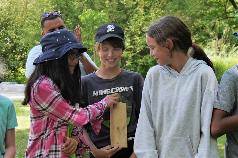 Three Junior Naturalists smile as they try to hide a block of wood from camp leaders view during a game.