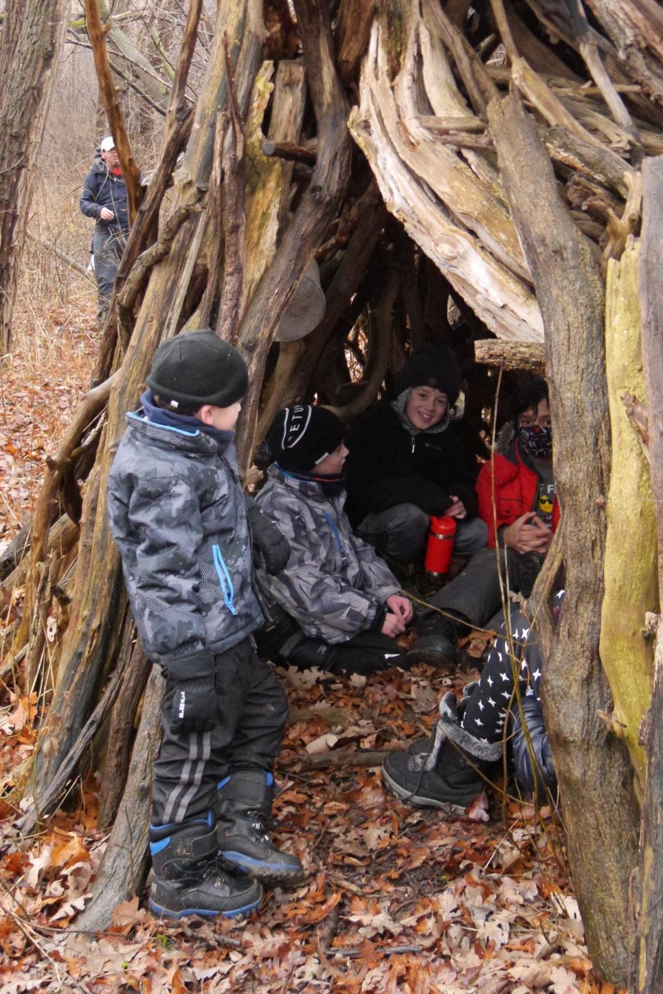 A group of children sit inside a fort made of sticks.