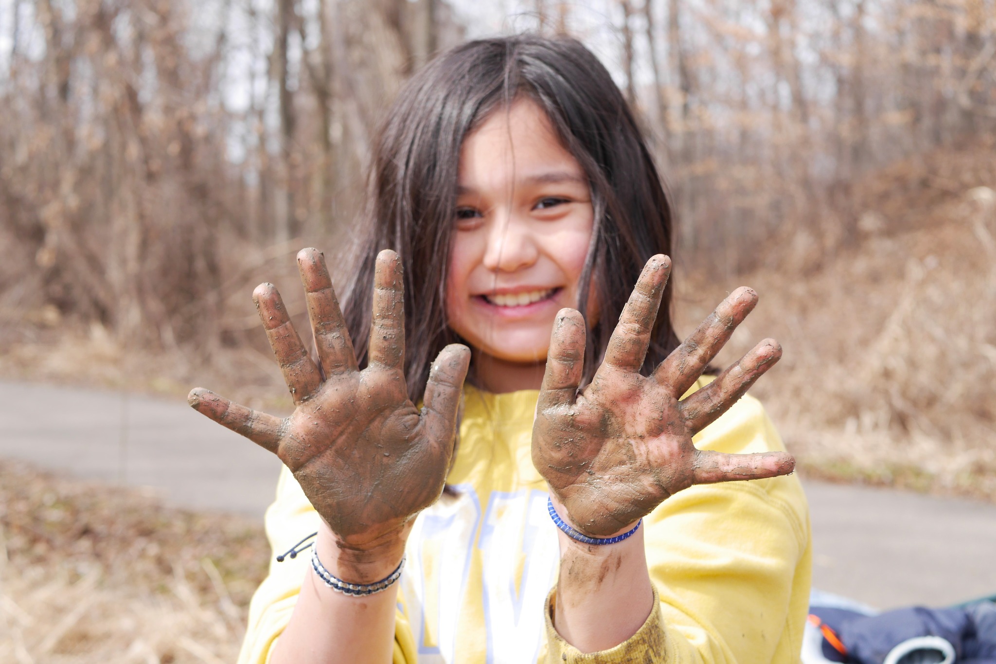 A smiling child shows their muddy hands to the camera