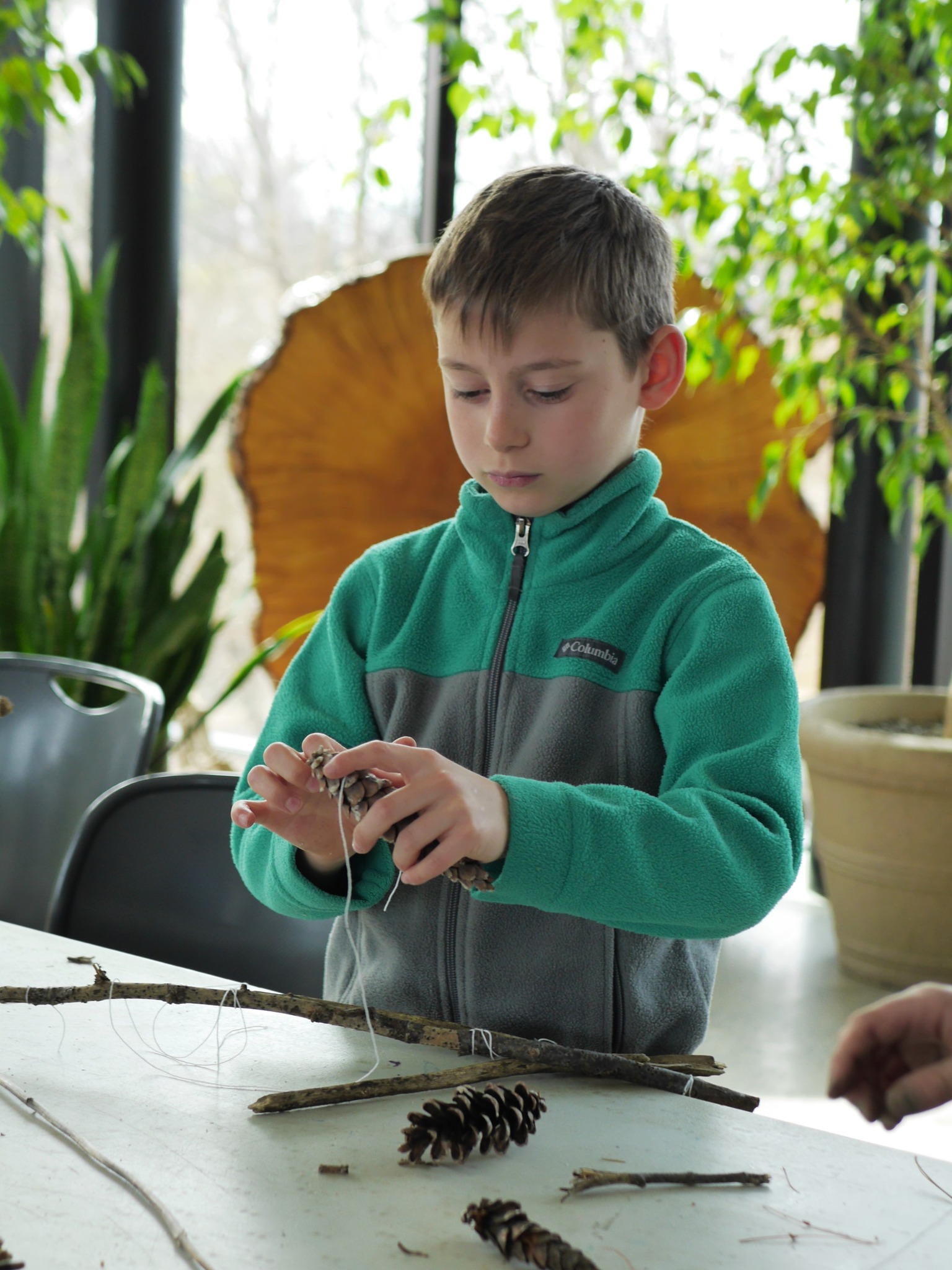 A child works on a craft using twine and pinecones