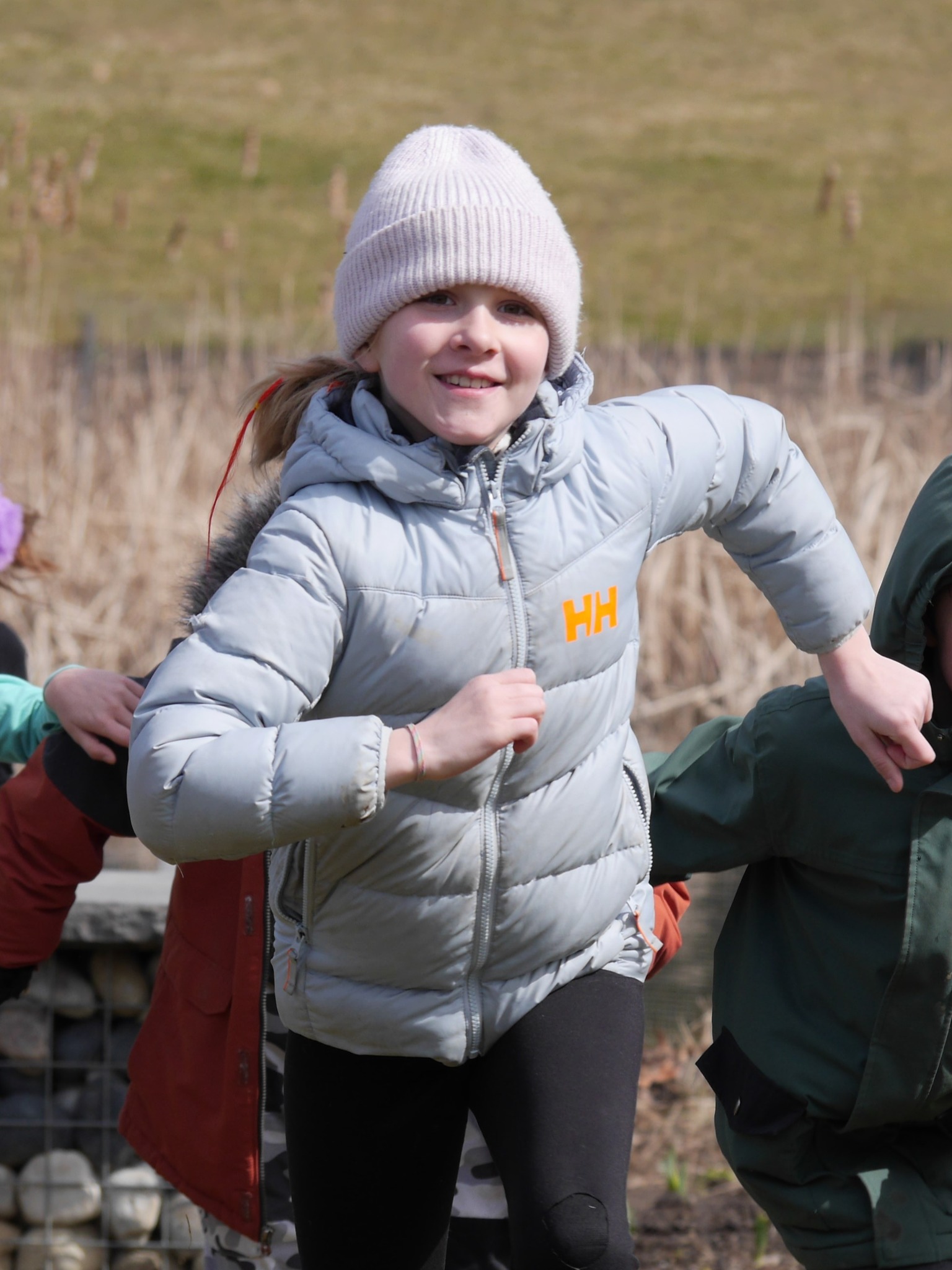 A smiling child wearing a winter coat runs across a garden lawn 