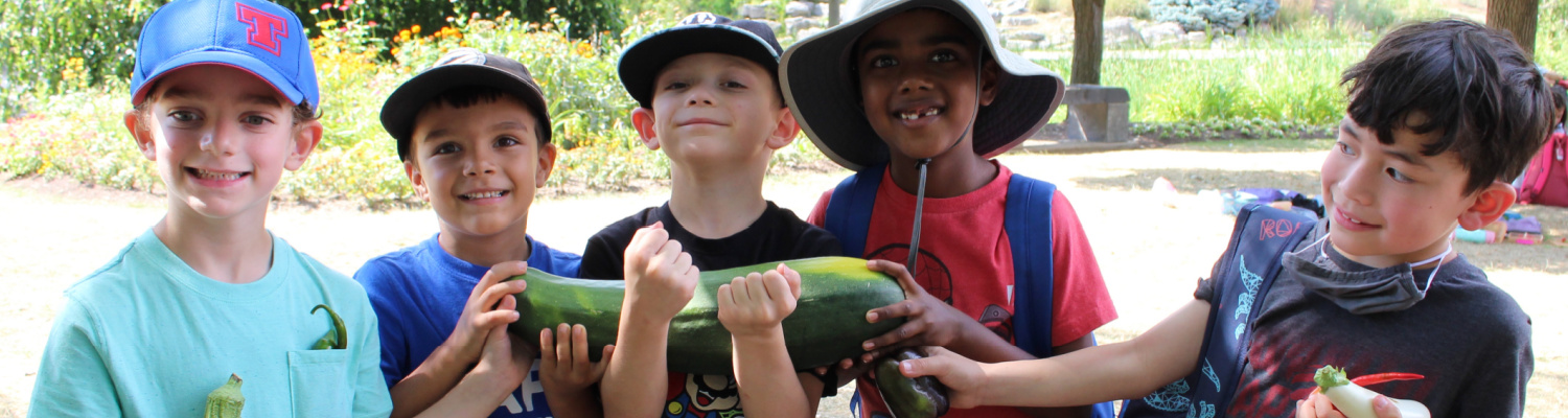 A row of campers smile as they hold up a zucchini from the Humber Food Learning Garden
