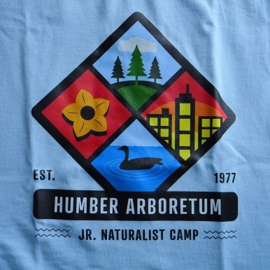 A blue Junior Naturalists t-shirt with a central crest featuring four images - trees, a city, a goose, and a flower
