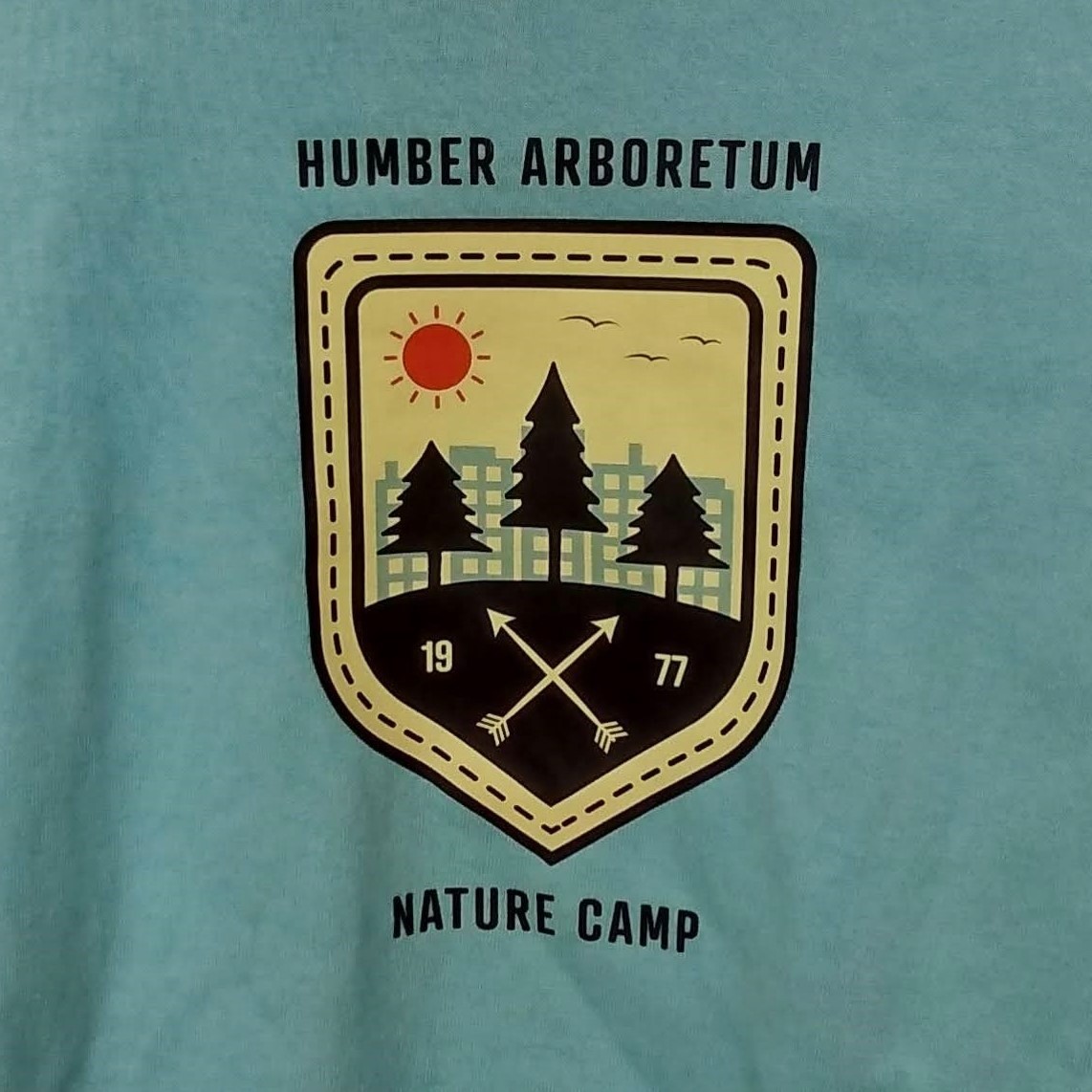 Close up of a Nature Camp t-shirt logo featuring trees in front of tall buildings 