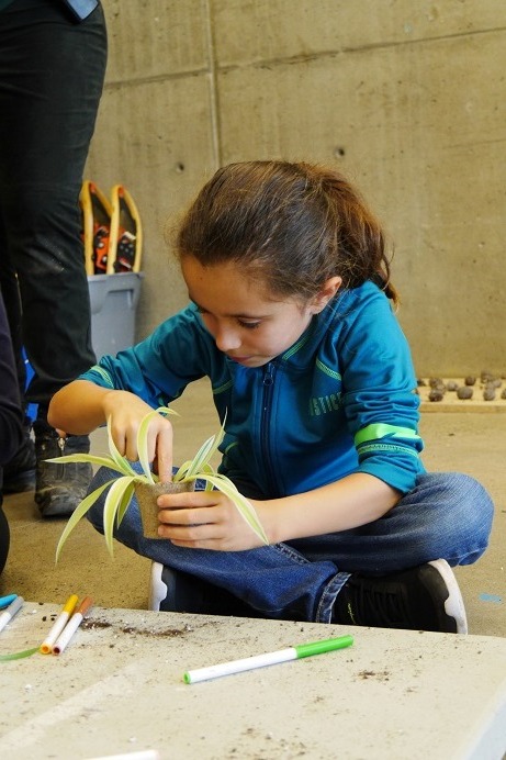 A girl sits on the floor of an education center, potting a spider plant.