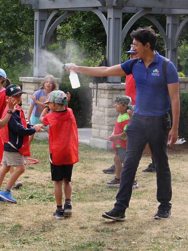 A camp leader spritzes kids with water on a summer day