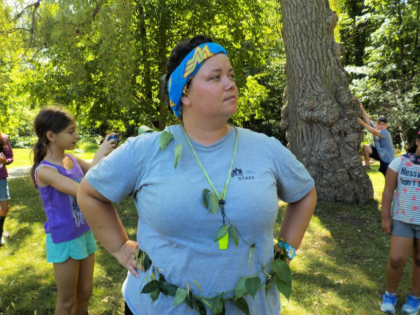 A counsellor draped in leaves stands in the Wonder Woman pose